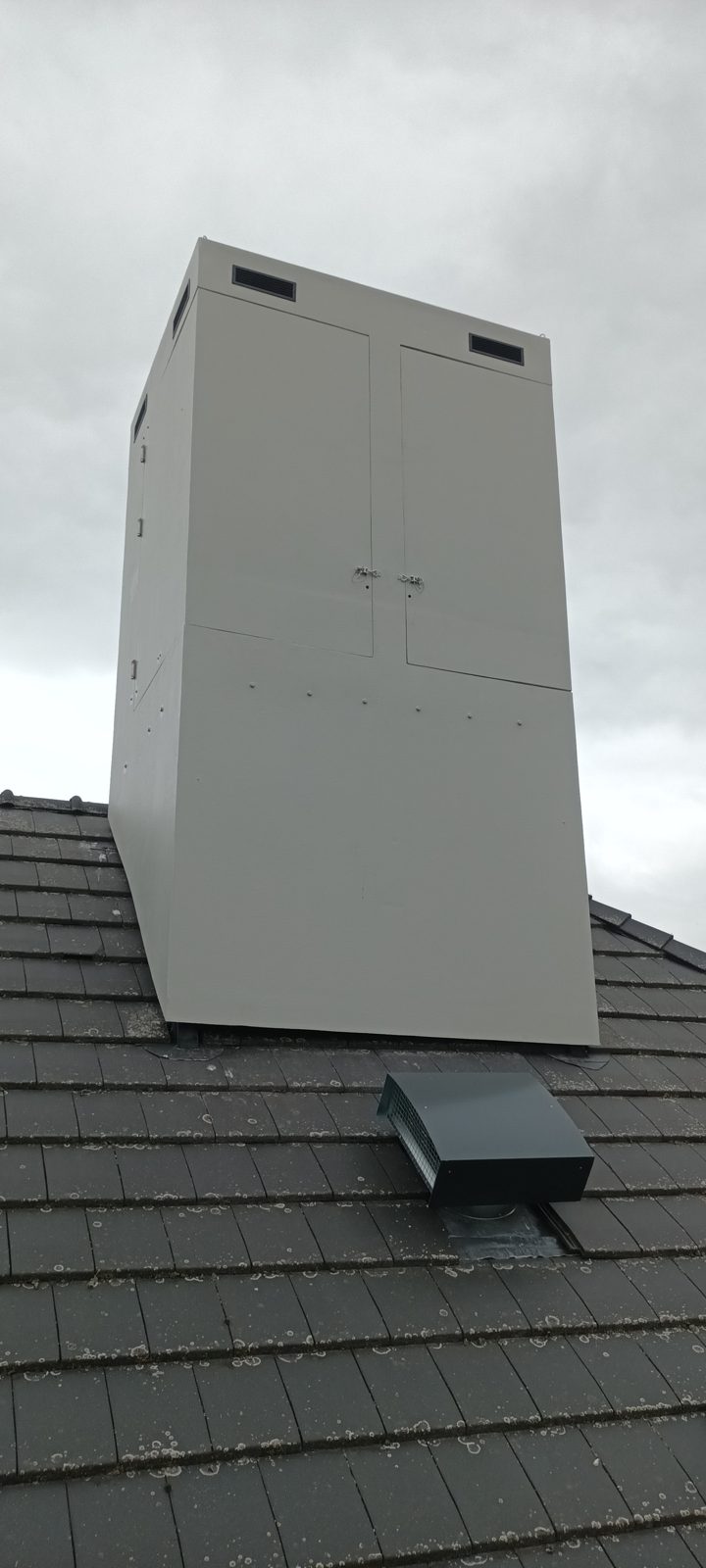 Fausse cheminée composite à double porte et grilles de ventilation sur toiture en tuiles