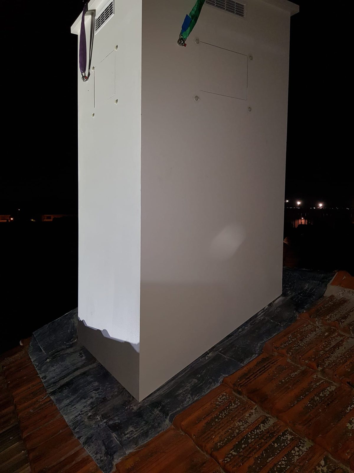 Fausse cheminée composite blanche avec grilles de ventilation et trappes d’accès, de nuit